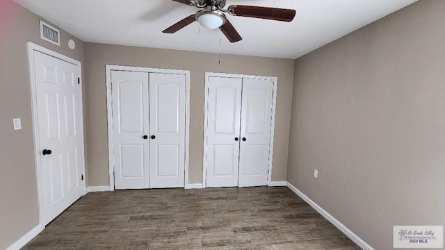 unfurnished bedroom featuring dark hardwood / wood-style flooring, two closets, and ceiling fan