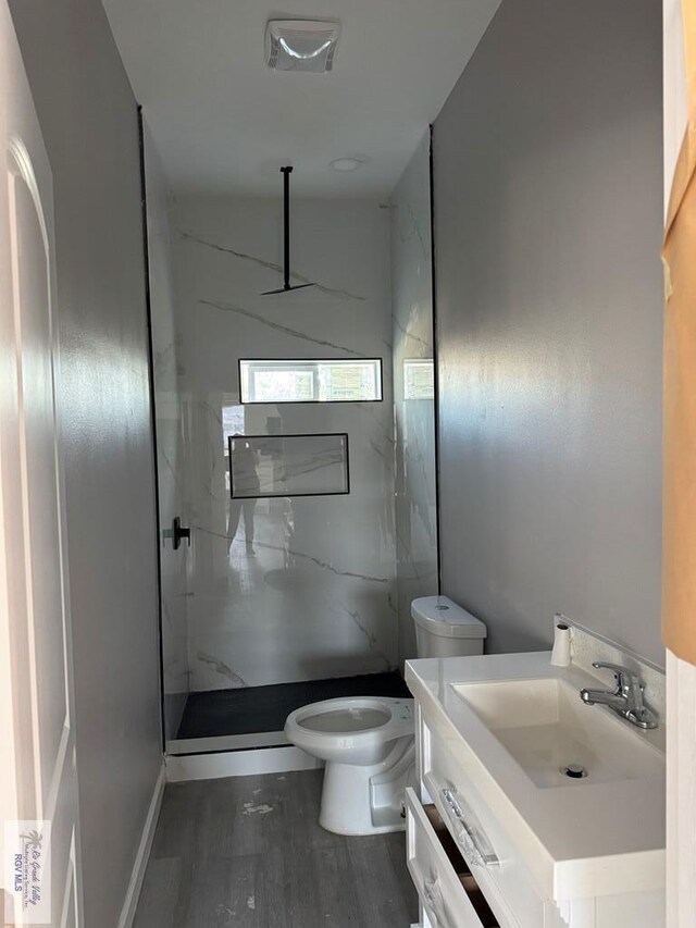 bathroom featuring a tile shower, hardwood / wood-style floors, vanity, and toilet