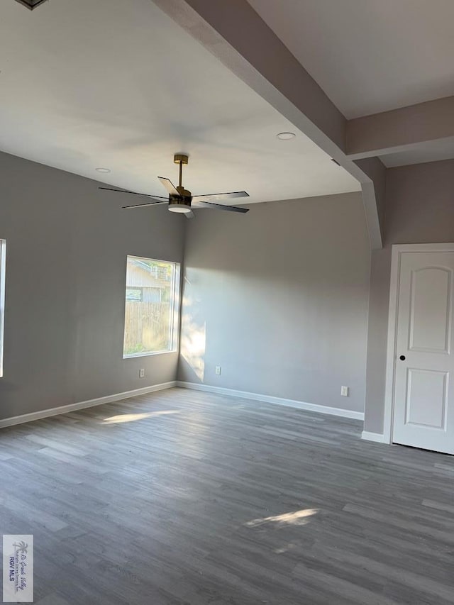 empty room with beamed ceiling, dark hardwood / wood-style flooring, and ceiling fan