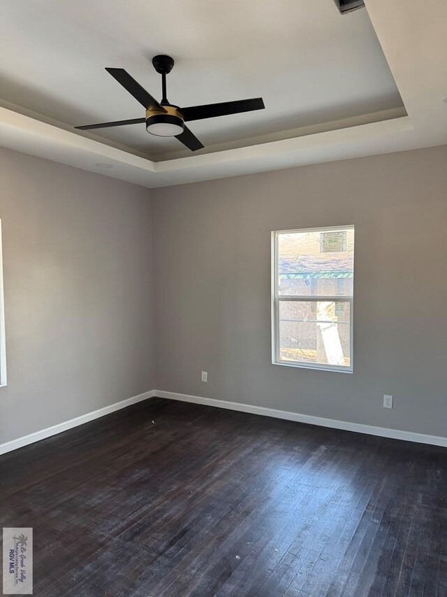 unfurnished room featuring ceiling fan, a raised ceiling, and dark wood-type flooring