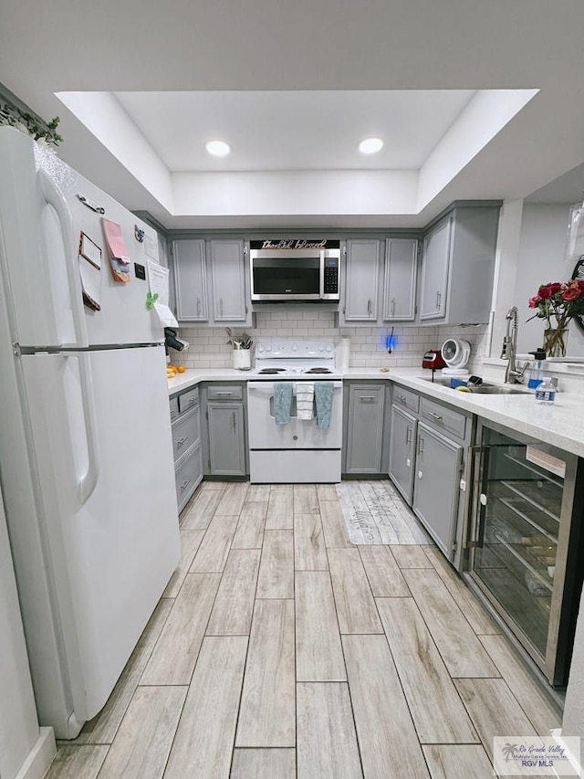 kitchen featuring gray cabinetry, a raised ceiling, white appliances, and wine cooler