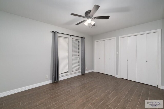 unfurnished bedroom featuring two closets, dark hardwood / wood-style floors, and ceiling fan