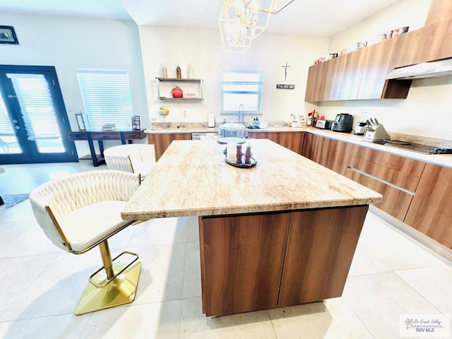 kitchen with a center island, a kitchen breakfast bar, stovetop, decorative light fixtures, and light tile patterned flooring