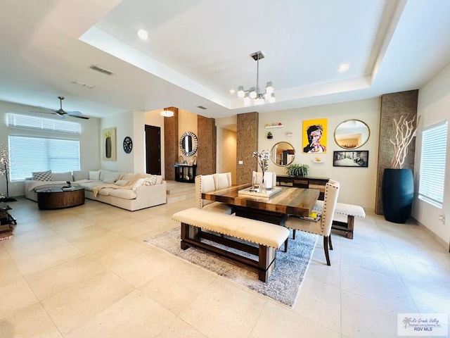 dining area featuring ceiling fan with notable chandelier, a raised ceiling, and a healthy amount of sunlight