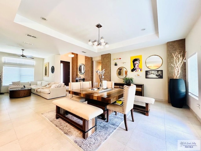 tiled dining space featuring ceiling fan with notable chandelier, a raised ceiling, and a wealth of natural light