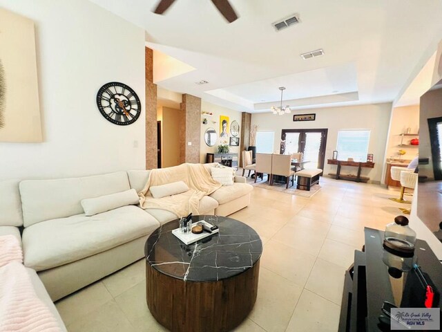 tiled living room with a tray ceiling and ceiling fan with notable chandelier