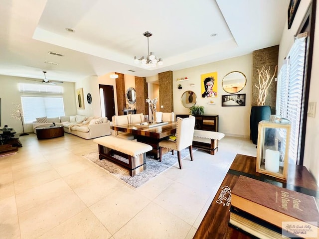 dining area with a tray ceiling and ceiling fan with notable chandelier