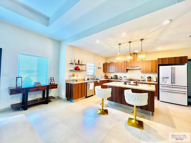 kitchen featuring stainless steel dishwasher, pendant lighting, white fridge with ice dispenser, a breakfast bar area, and an island with sink