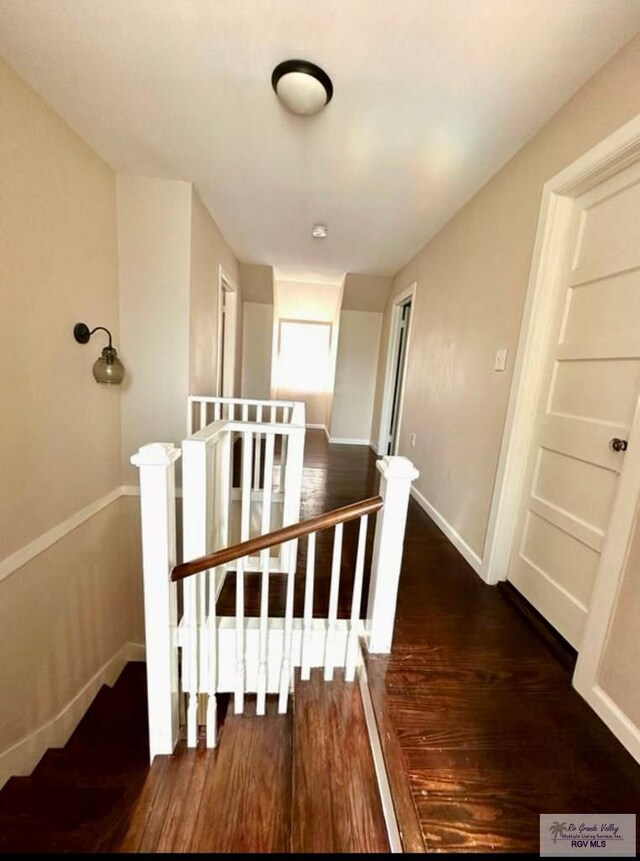 corridor featuring baseboards, an upstairs landing, and wood finished floors