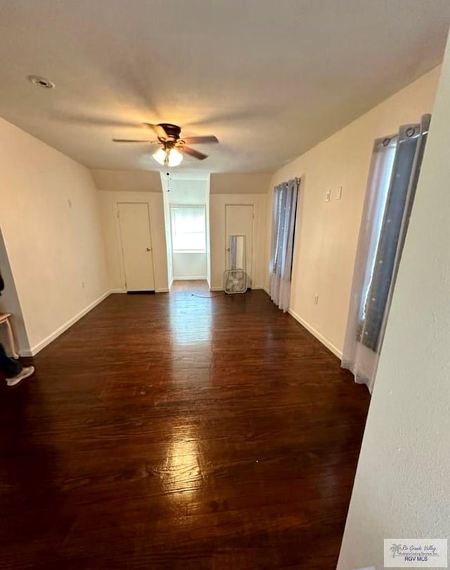 unfurnished living room with a ceiling fan, dark wood-type flooring, and baseboards