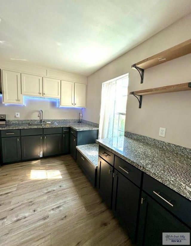 kitchen with a sink, light wood-style flooring, white cabinets, and dark stone countertops