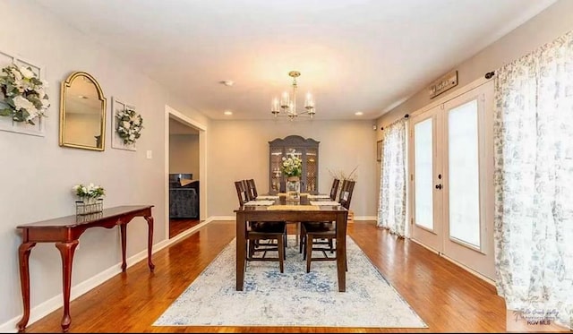 dining space with french doors, baseboards, an inviting chandelier, and wood finished floors