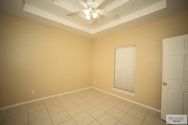 empty room featuring ceiling fan, a raised ceiling, and light tile patterned floors