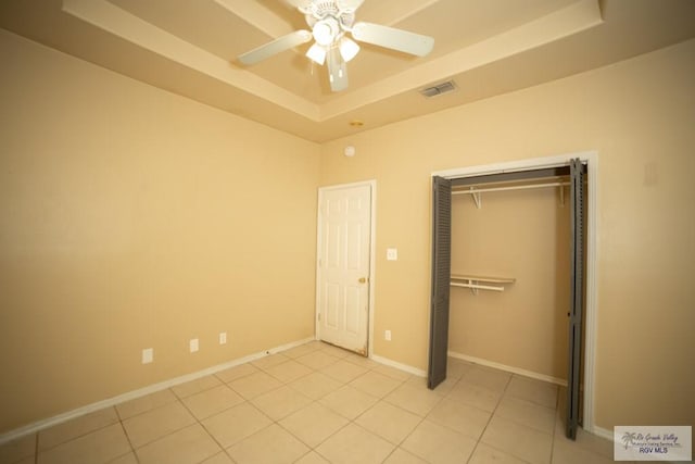 unfurnished bedroom featuring a tray ceiling, ceiling fan, a closet, and light tile patterned flooring