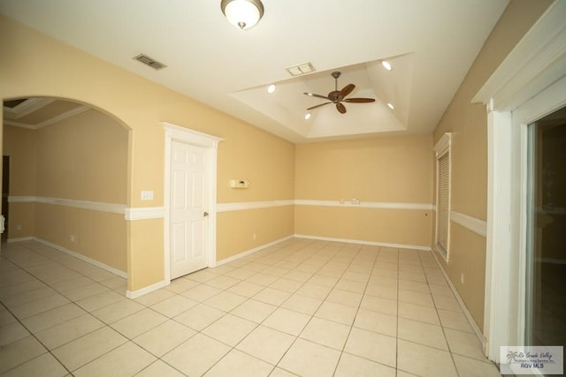 empty room with a tray ceiling, ceiling fan, crown molding, and light tile patterned floors