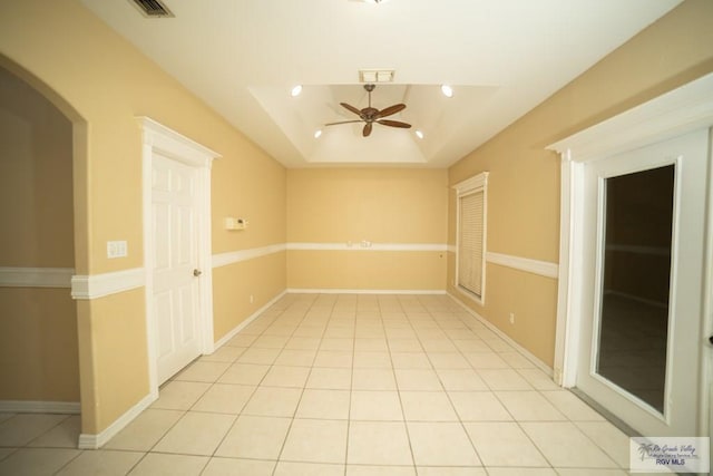 empty room featuring a tray ceiling, ceiling fan, and light tile patterned floors