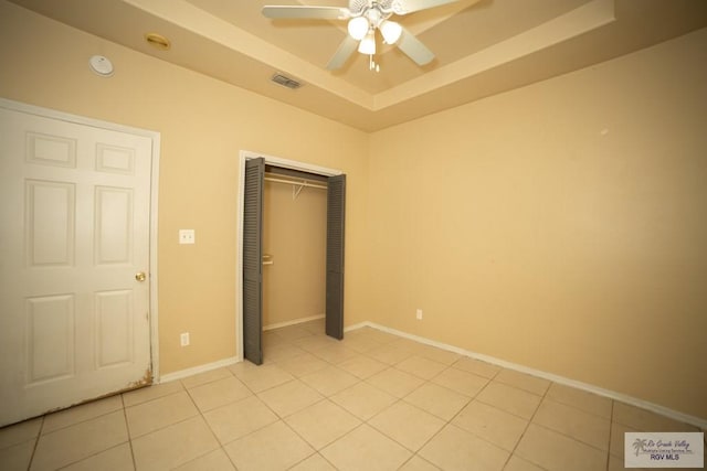 unfurnished bedroom with light tile patterned floors, a closet, a raised ceiling, and ceiling fan