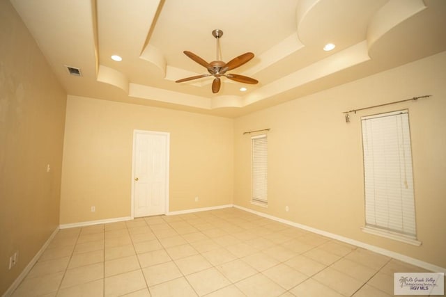 tiled spare room with ceiling fan and a raised ceiling