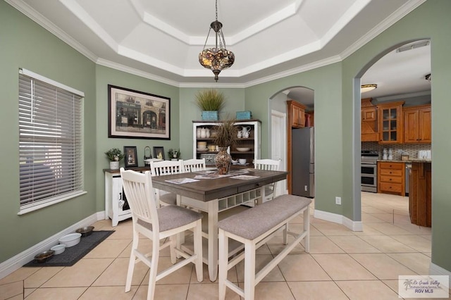 dining area with light tile patterned floors, ornamental molding, and a tray ceiling