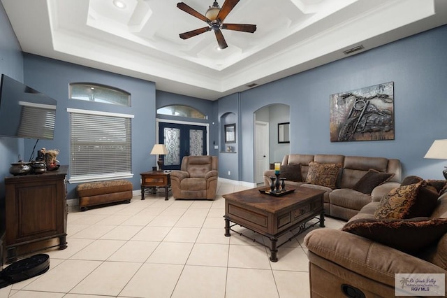 living room with a raised ceiling, ceiling fan, and light tile patterned flooring