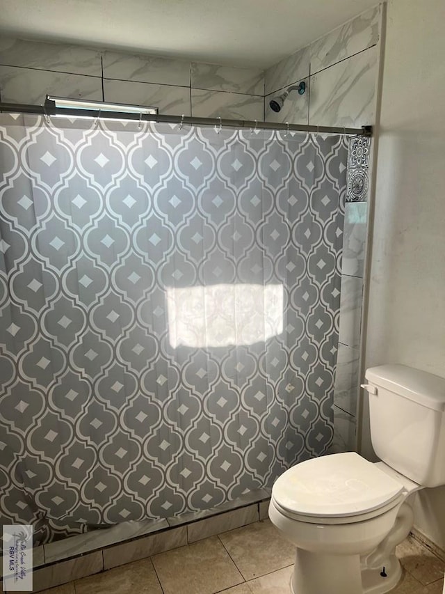 bathroom with tile patterned flooring, tiled shower, and toilet