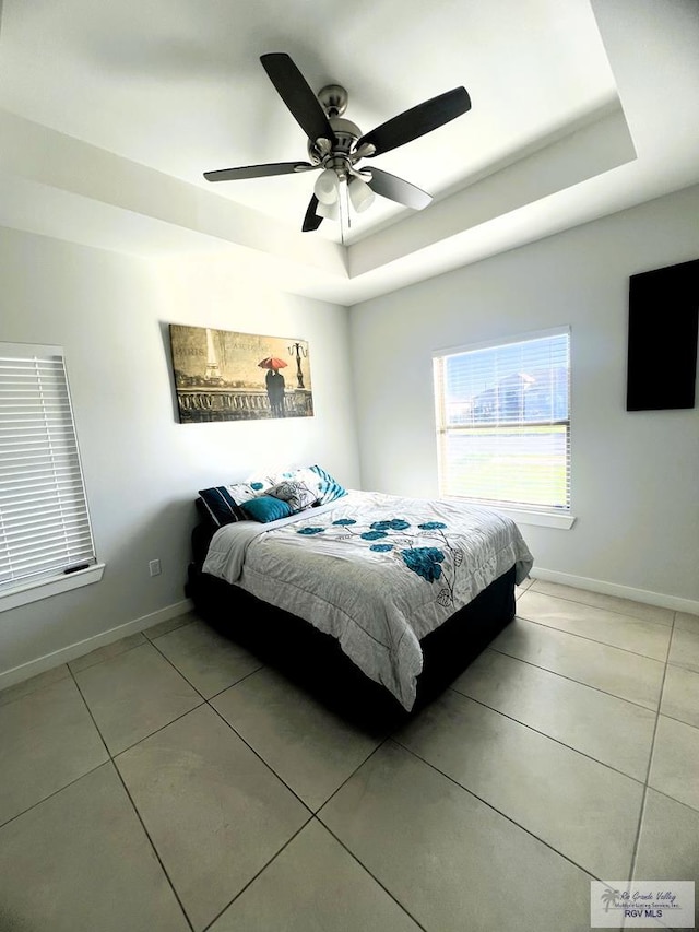 tiled bedroom with ceiling fan and a tray ceiling