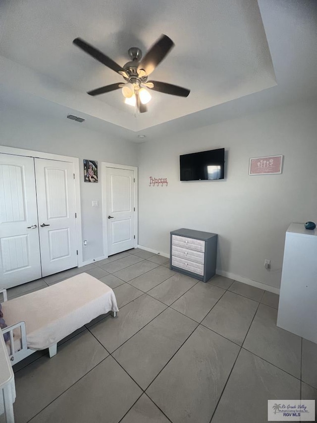 tiled bedroom with ceiling fan, a raised ceiling, and a closet