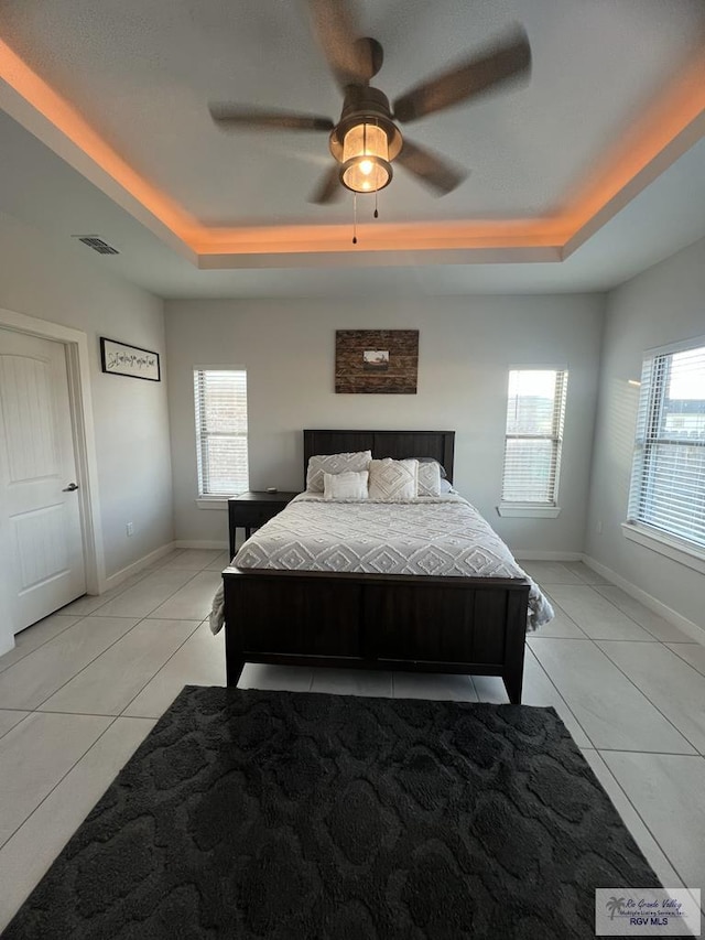 bedroom with ceiling fan, light tile patterned floors, a tray ceiling, and multiple windows