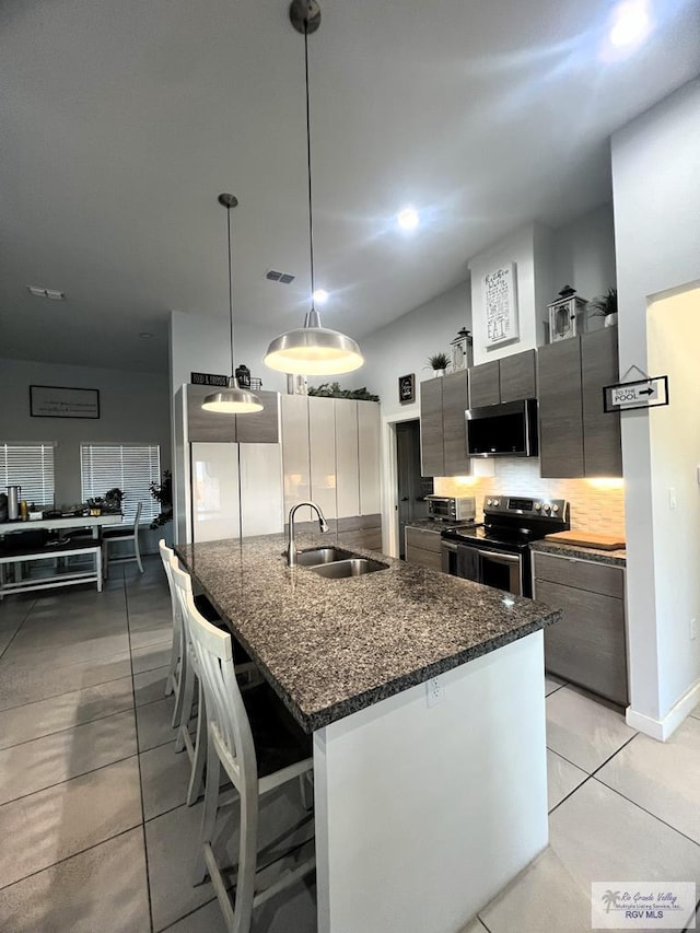 kitchen featuring appliances with stainless steel finishes, backsplash, sink, decorative light fixtures, and a breakfast bar area