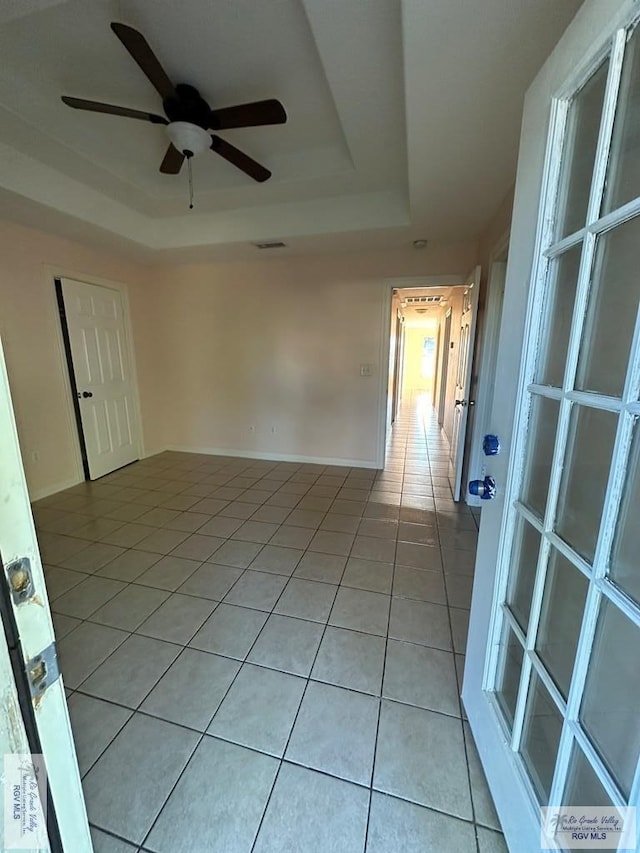spare room featuring ceiling fan, a tray ceiling, and light tile patterned floors