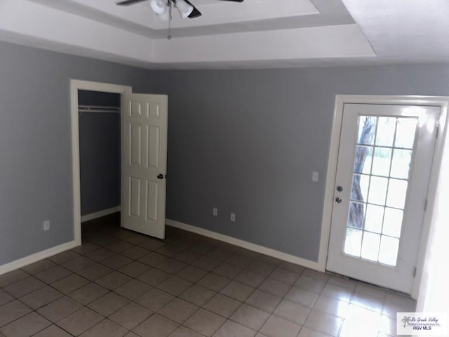 interior space with a raised ceiling, a ceiling fan, and baseboards