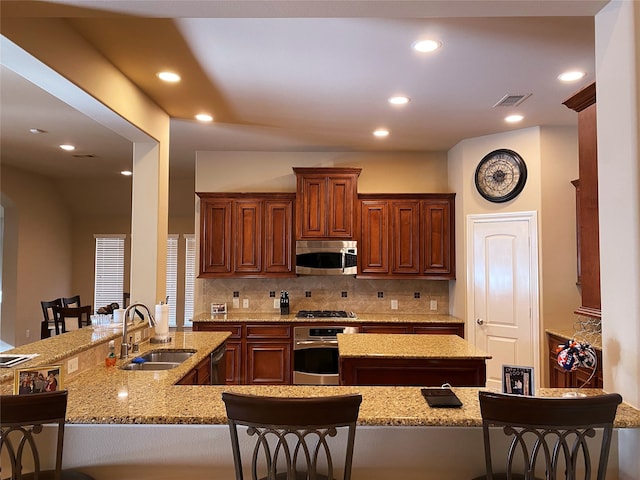 kitchen featuring a breakfast bar, kitchen peninsula, light stone countertops, stainless steel appliances, and sink