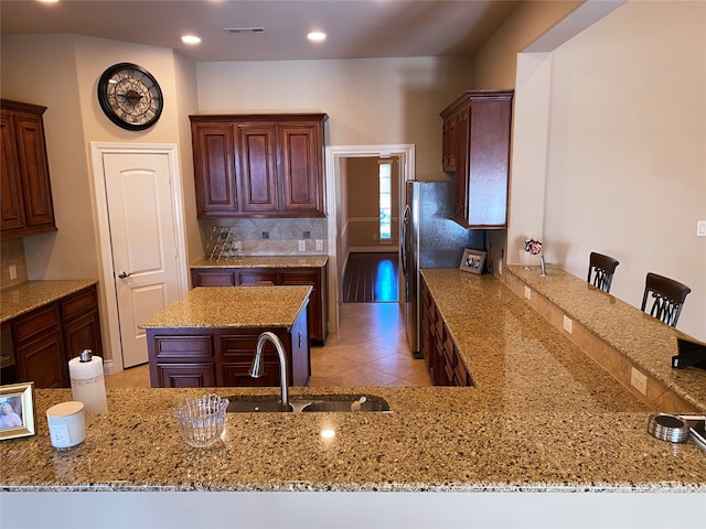 kitchen featuring a breakfast bar, light stone counters, tasteful backsplash, sink, and kitchen peninsula