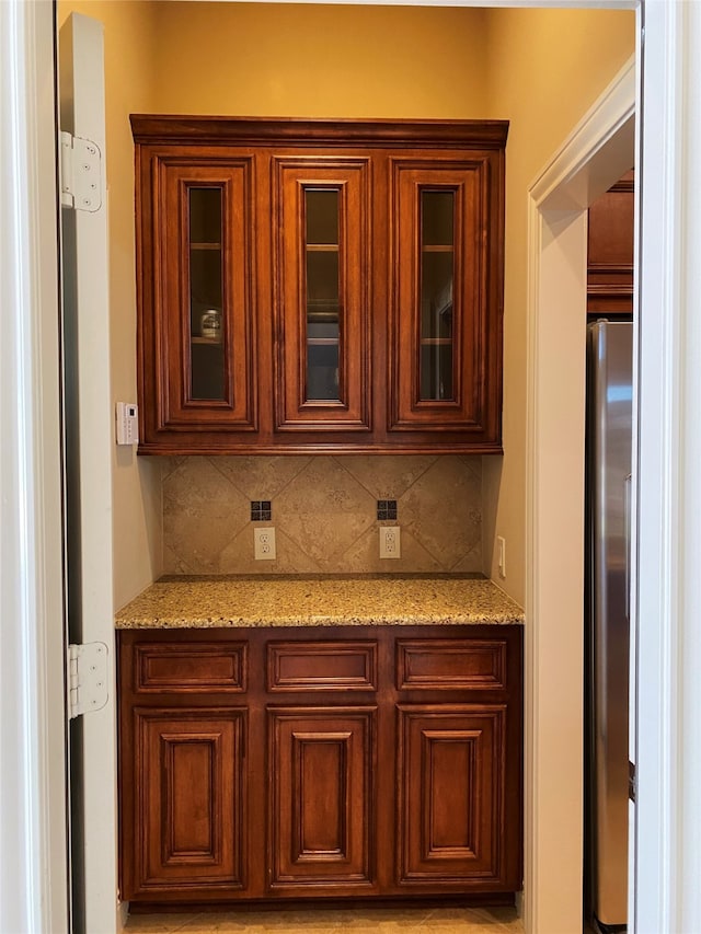 kitchen with stainless steel fridge, backsplash, and light stone counters