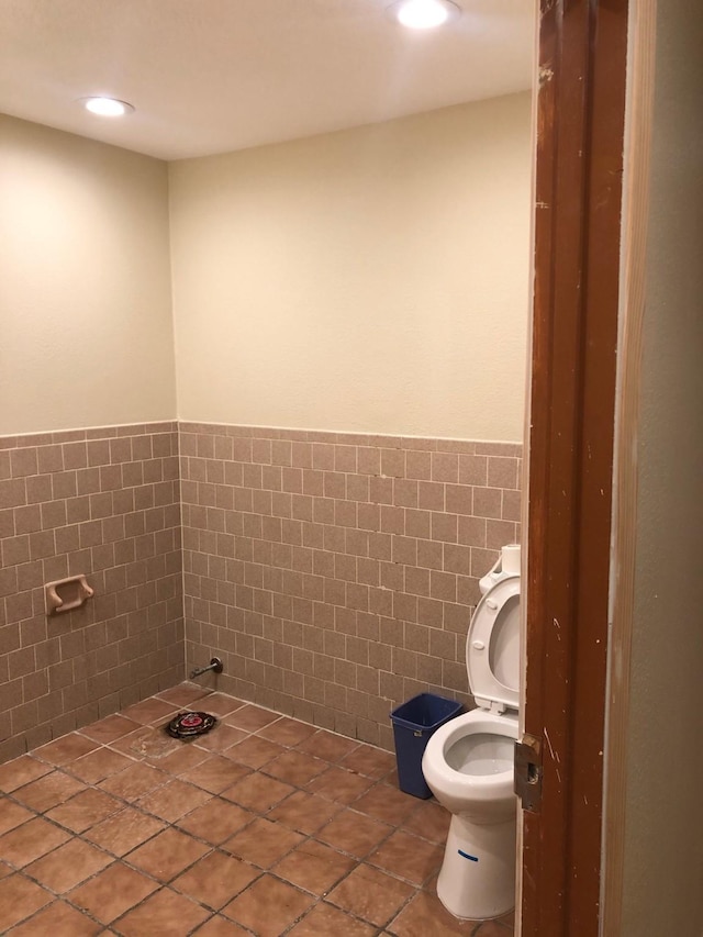 bathroom with tile flooring, toilet, and tile walls