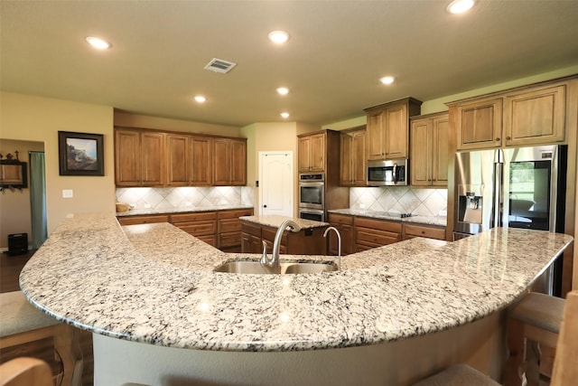 kitchen with stainless steel appliances, a kitchen bar, a large island with sink, backsplash, and sink