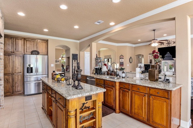 kitchen featuring ceiling fan, light stone counters, crown molding, a kitchen island, and stainless steel appliances