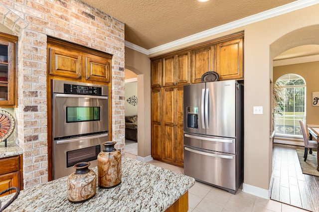 kitchen with crown molding, light stone countertops, stainless steel appliances, and a textured ceiling