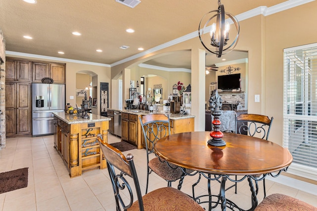 tiled dining room with ceiling fan with notable chandelier, sink, a brick fireplace, a textured ceiling, and ornamental molding