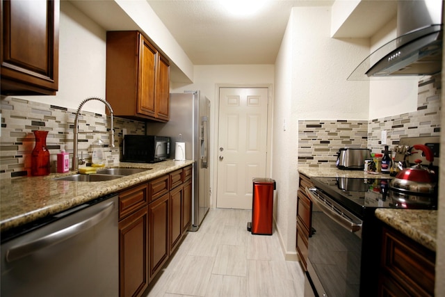 kitchen featuring tasteful backsplash, wall chimney range hood, light stone counters, stainless steel appliances, and sink