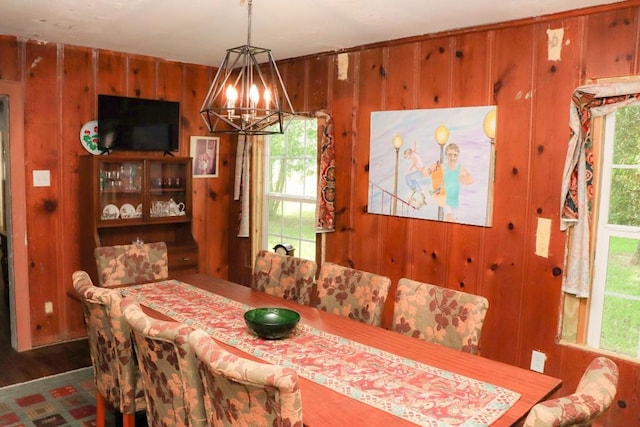 dining area with plenty of natural light, an inviting chandelier, dark hardwood / wood-style flooring, and wood walls