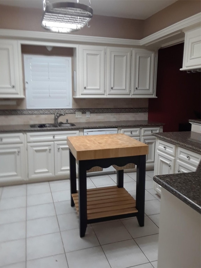 kitchen featuring dark stone countertops, light tile floors, sink, white dishwasher, and white cabinets