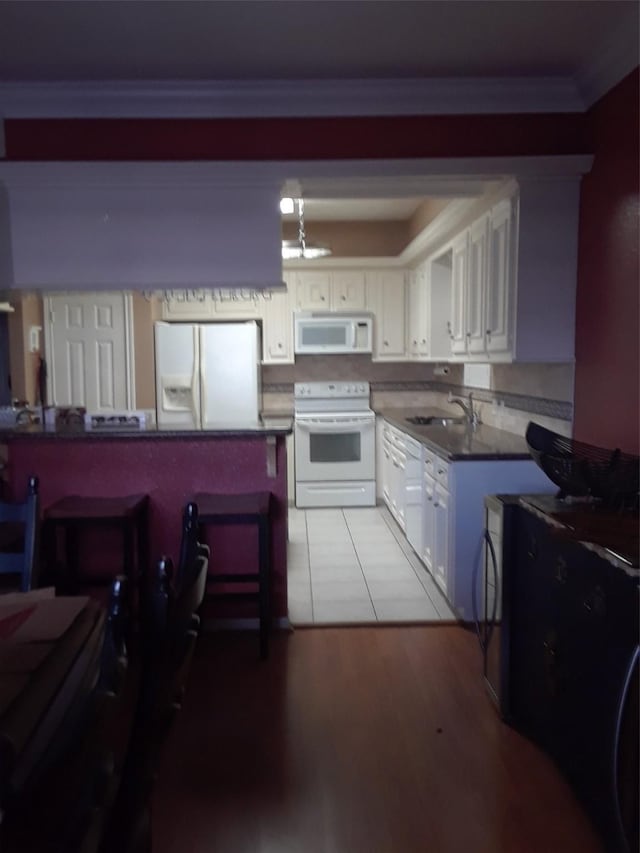 kitchen featuring white cabinetry, white appliances, light hardwood / wood-style floors, sink, and a breakfast bar area