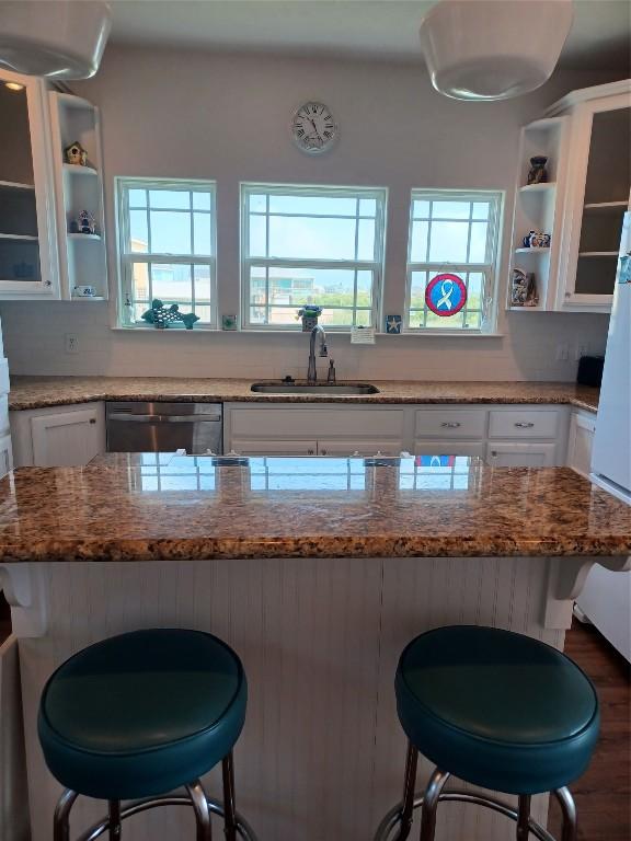 kitchen featuring white cabinetry, sink, light stone counters, dishwasher, and a breakfast bar area