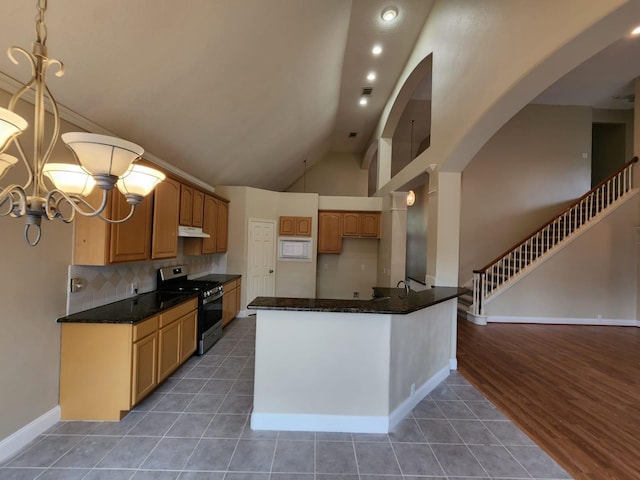 kitchen with dark tile floors, a chandelier, stainless steel gas stove, tasteful backsplash, and pendant lighting