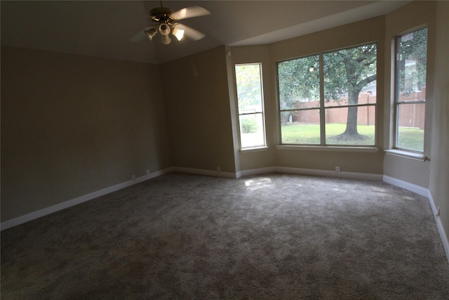 empty room featuring ceiling fan, dark colored carpet, and a wealth of natural light