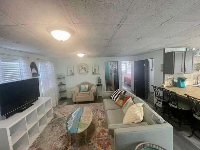 living room featuring a paneled ceiling, sink, and hardwood / wood-style flooring