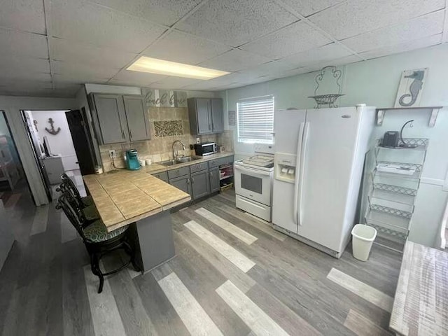 kitchen with dark hardwood / wood-style floors, white appliances, sink, tasteful backsplash, and gray cabinets