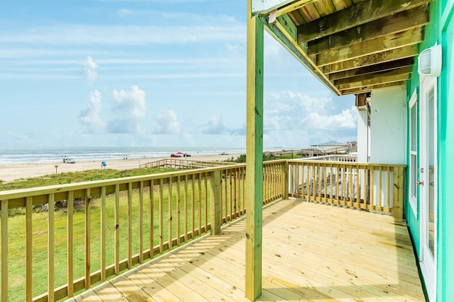 wooden deck with a water view, a view of the beach, and a lawn