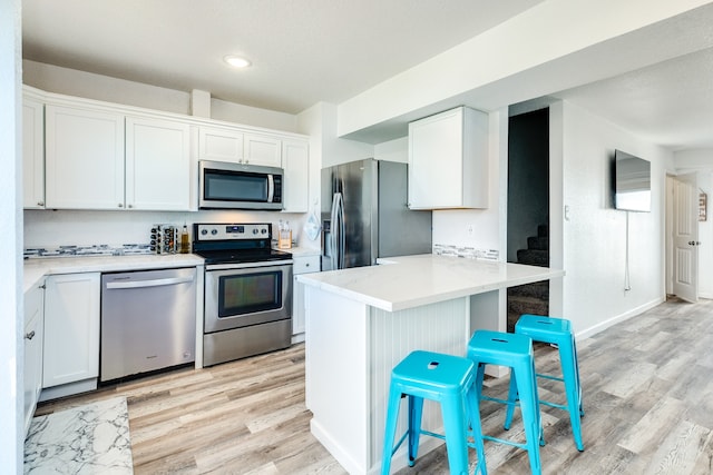 kitchen with white cabinets, a kitchen bar, light hardwood / wood-style floors, and appliances with stainless steel finishes